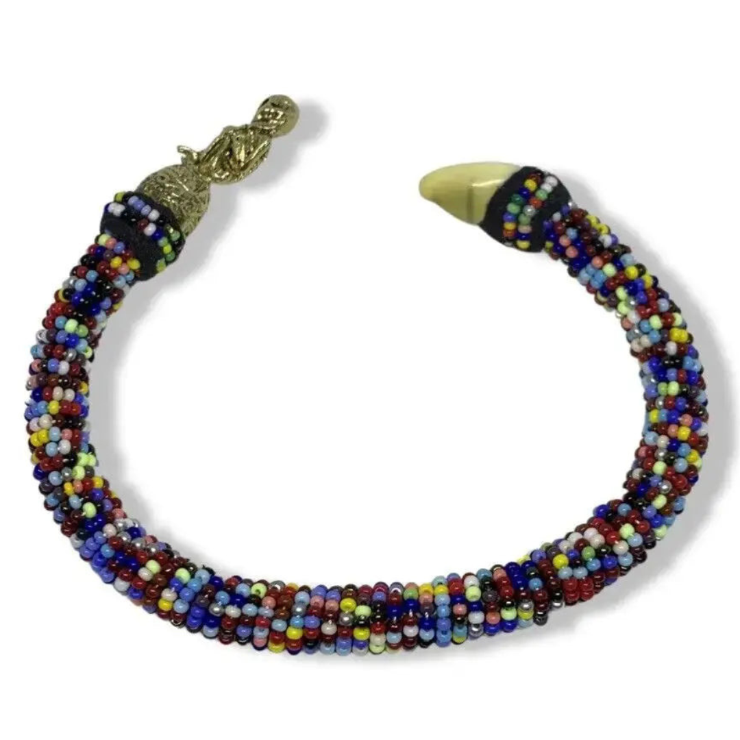 The Ilde bracelet by SanteriaGuide is a vibrant beaded accessory inspired by the Orishas, featuring a bronze clasp and a mother-of-pearl charm. The beads, arranged in a diverse array of colors, create an intricate pattern, while the bronze clasp adds an elegant touch to this Santos bracelet's overall design.