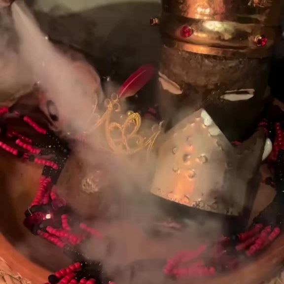 Elegua adorned with a metallic crown and a handmade mazo with smoke swirling around
